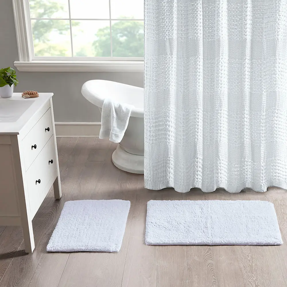 White bathroom interior with shower curtain and rugs.