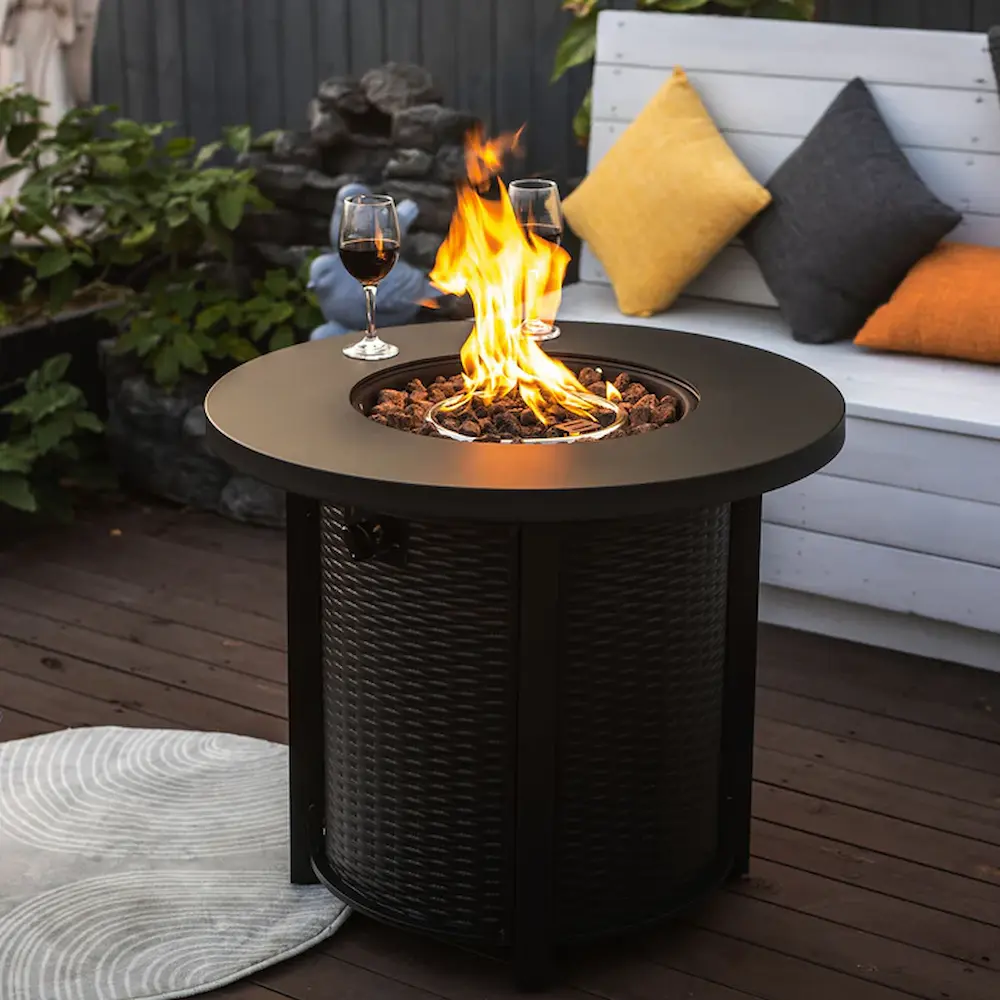 Outdoor fire pit table with burning flame and wine glasses.