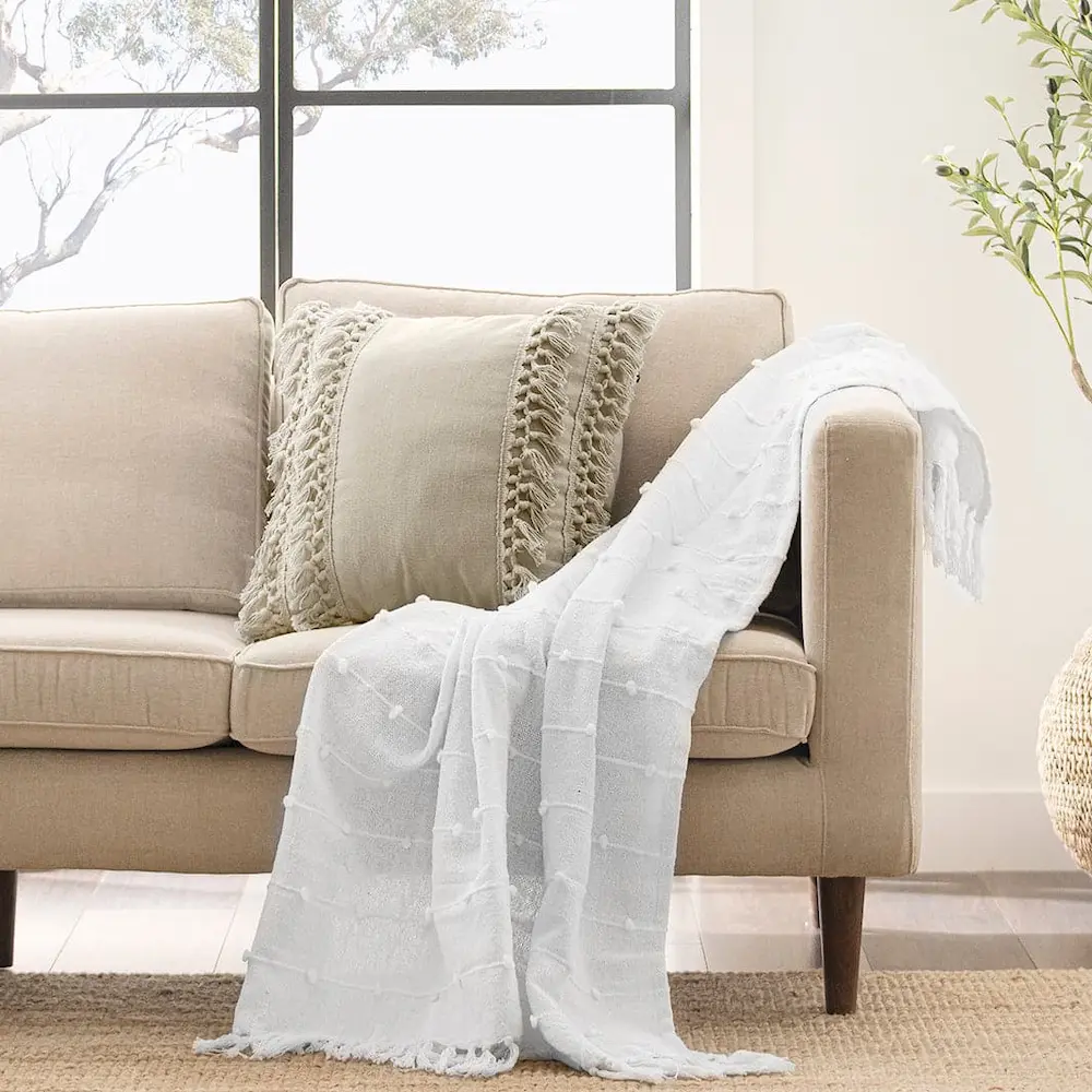 Beige sofa with decorative pillows and white throw blanket.